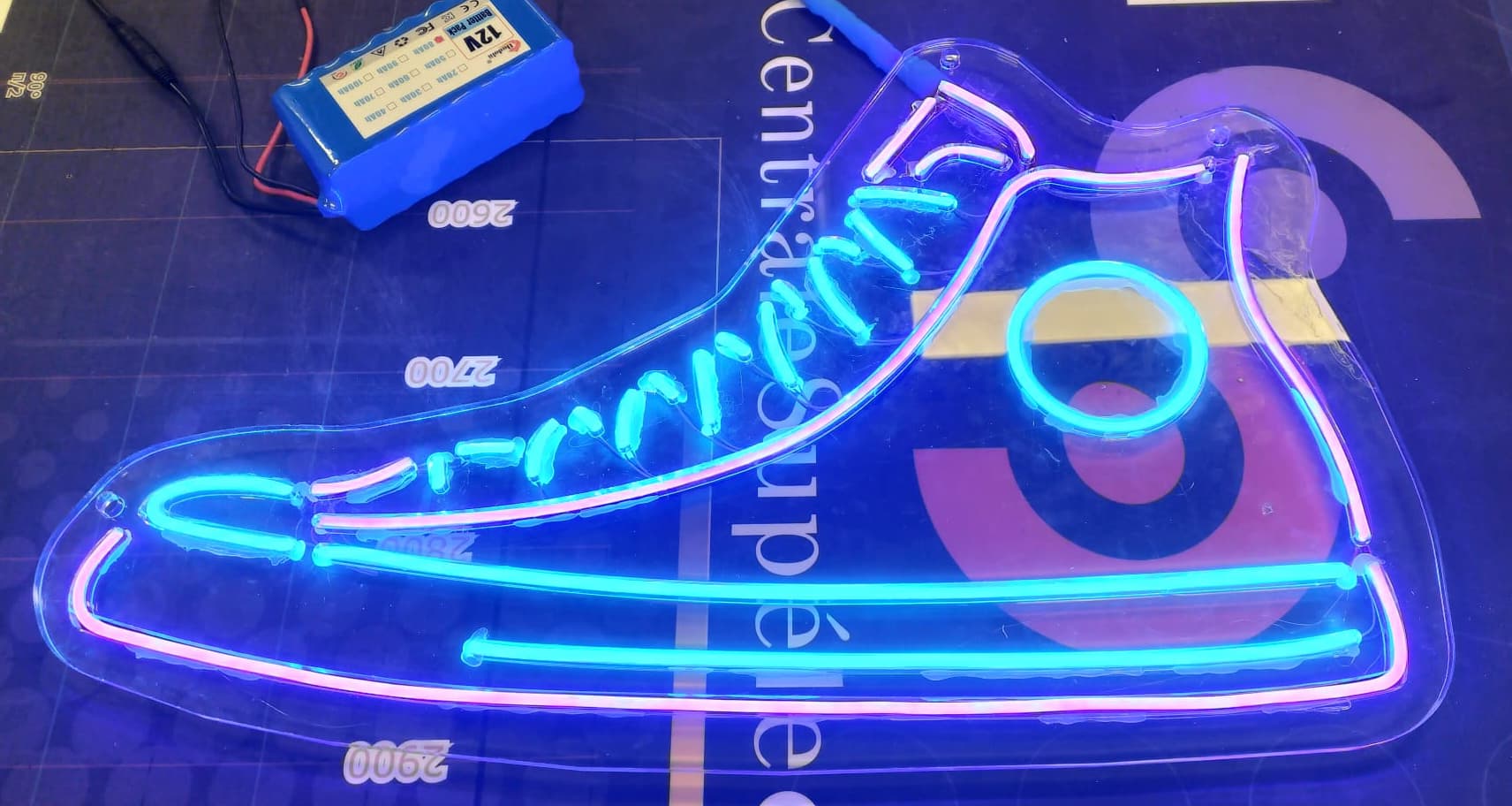 Enseigne LED en forme de basket stylisée, éclairée en bleu et rose, posée sur une table de travail.
