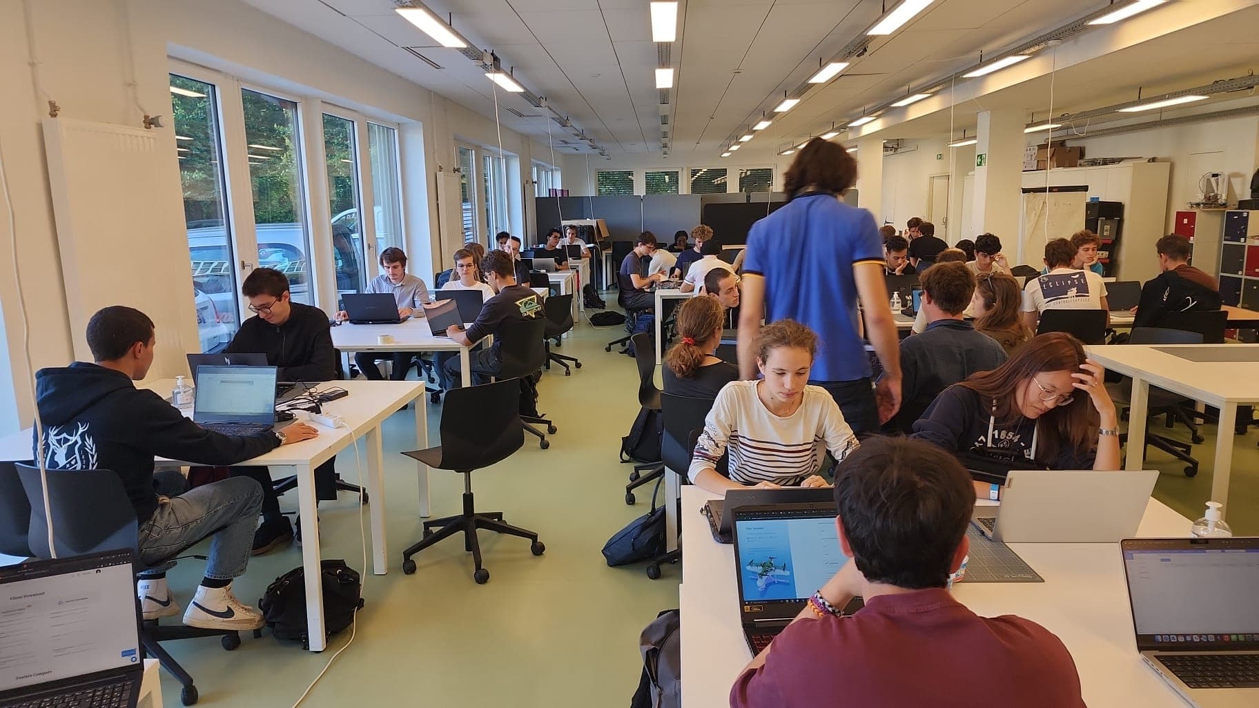 Salle remplie d’étudiants travaillant en binômes ou petits groupes sur des ordinateurs portables, pendant une session de formation organisée par le Club Tech dans la halle technique.