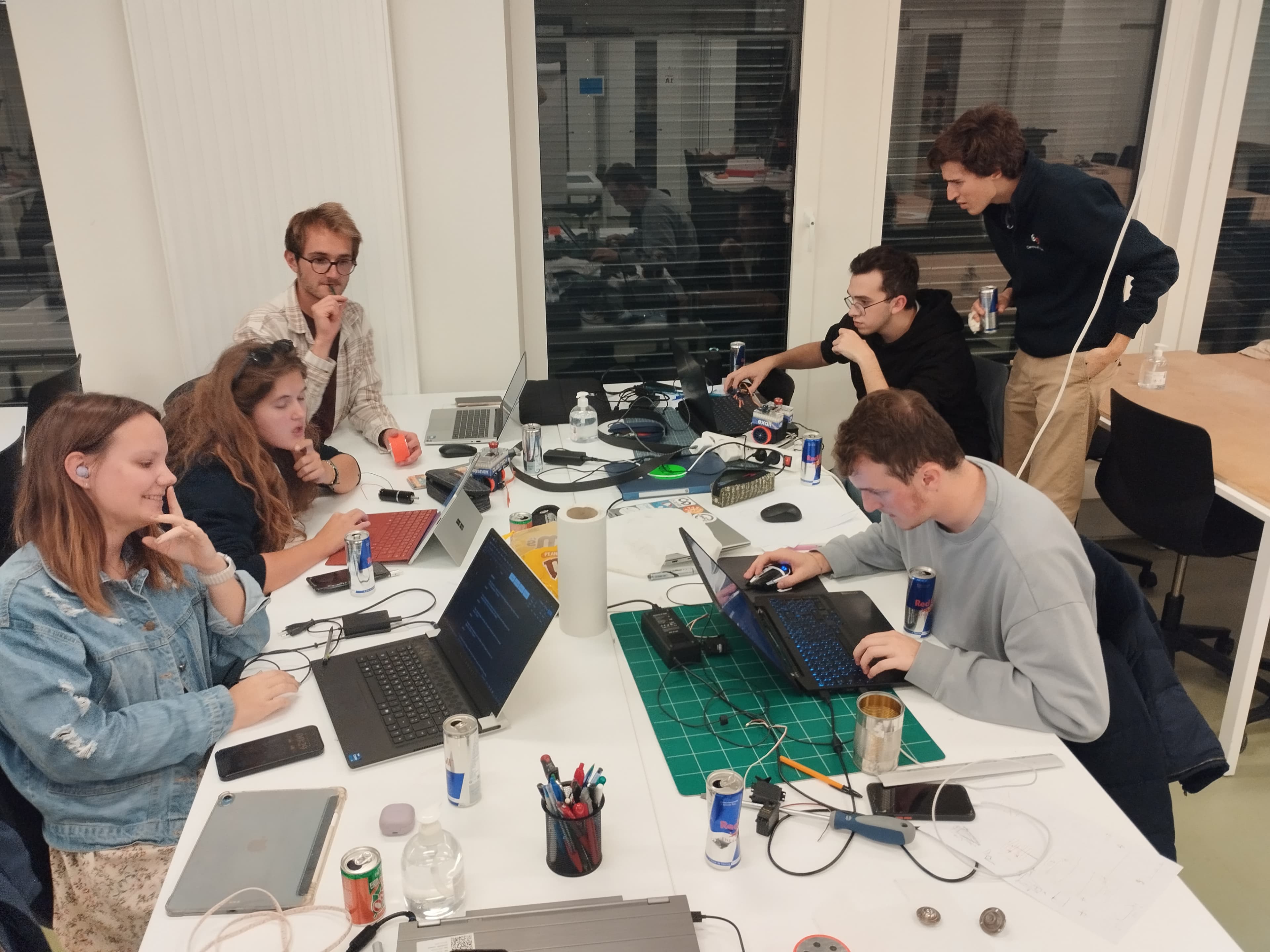 Étudiants de première année réunis autour d’une table, travaillant sur un robot pendant le hackathon dans la halle technique de CentraleSupélec, avec ordinateurs, outils et composants électroniques.