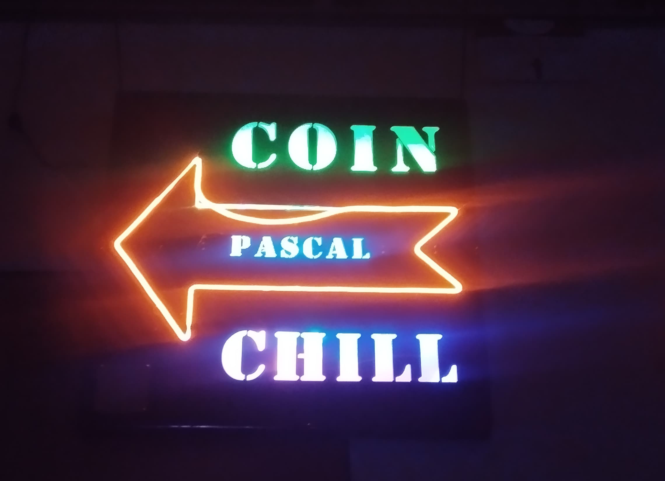 Panneau lumineux 'COIN PASCAL CHILL' avec une flèche orange pointant à gauche, dans une ambiance tamisée.