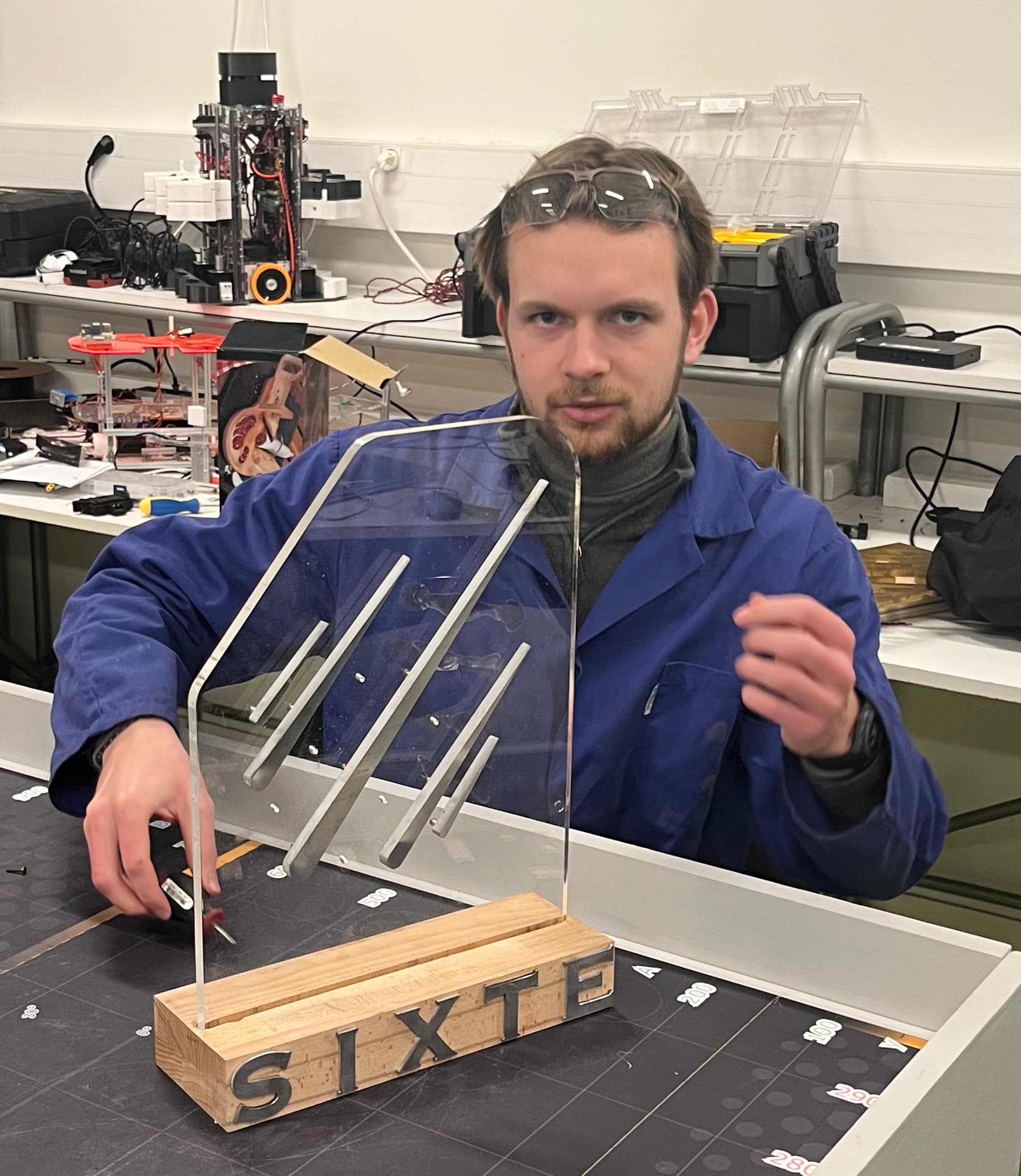 Jeune homme en blouse tenant un trophée du tournoi SIXTE en plexiglas, monté sur une base en bois gravée.